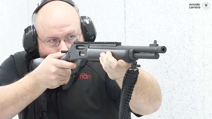 Man in black shirt and shooting gear shooting a lever-action rifle on white shooting range.