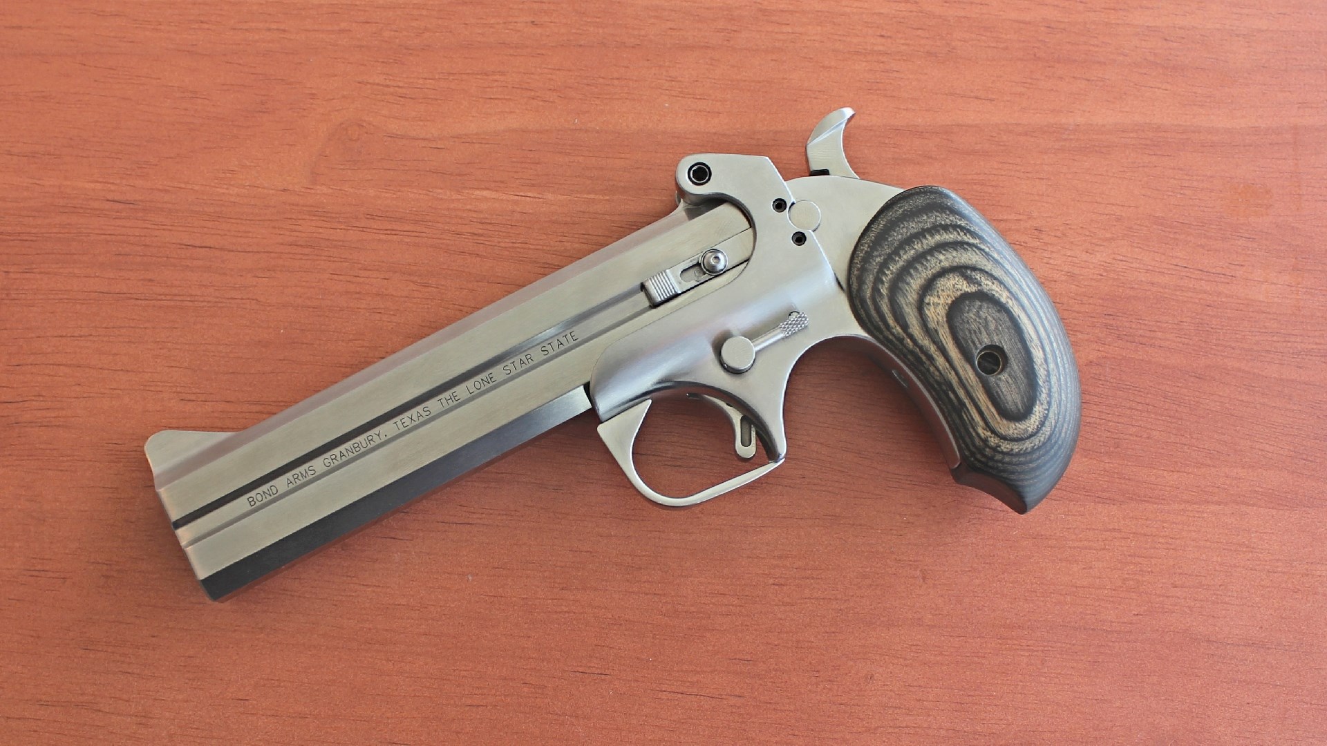 Left side of a long-barreled Bond Arms derringer on a wood table.