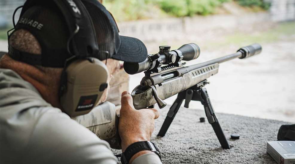 Savage Arms Axis 2 bolt-action rifle with suppressor shooting range man hat earmuffs