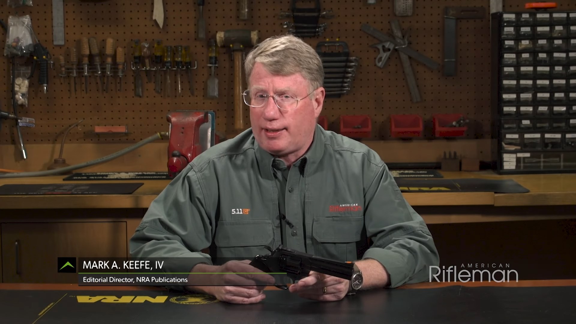 Mark A. Keefe, IV, Editorial Director sitting at workbench with Colt Python revolver in hand talking to camera. Screenshot from YouTube video.