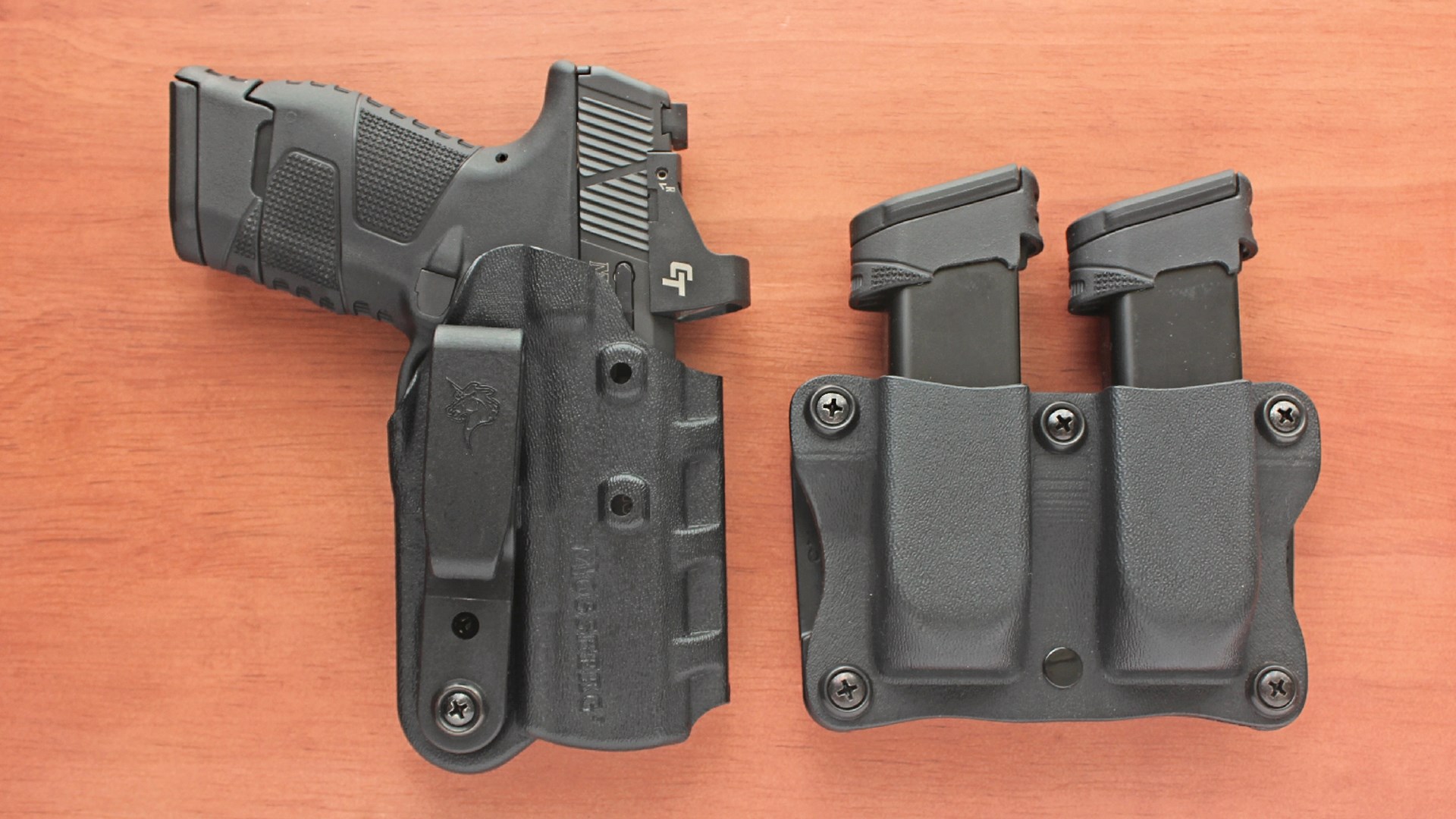 DeSantis Holster for black handgun with red-dot optic and magazine pouches loaded with mags shown on wood table