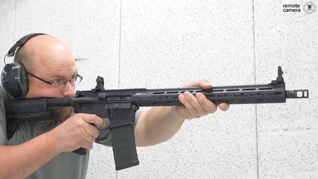 Man in gray shirt with hearing protection shooting a Springfield Armory Saint Victor in a white shooting range.