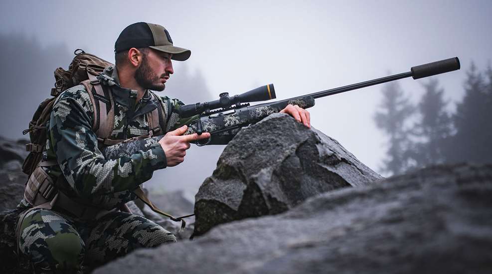Bearded, camouflaged hunter aiming the Springfield Armory Model 2020 Boundary over a rock.