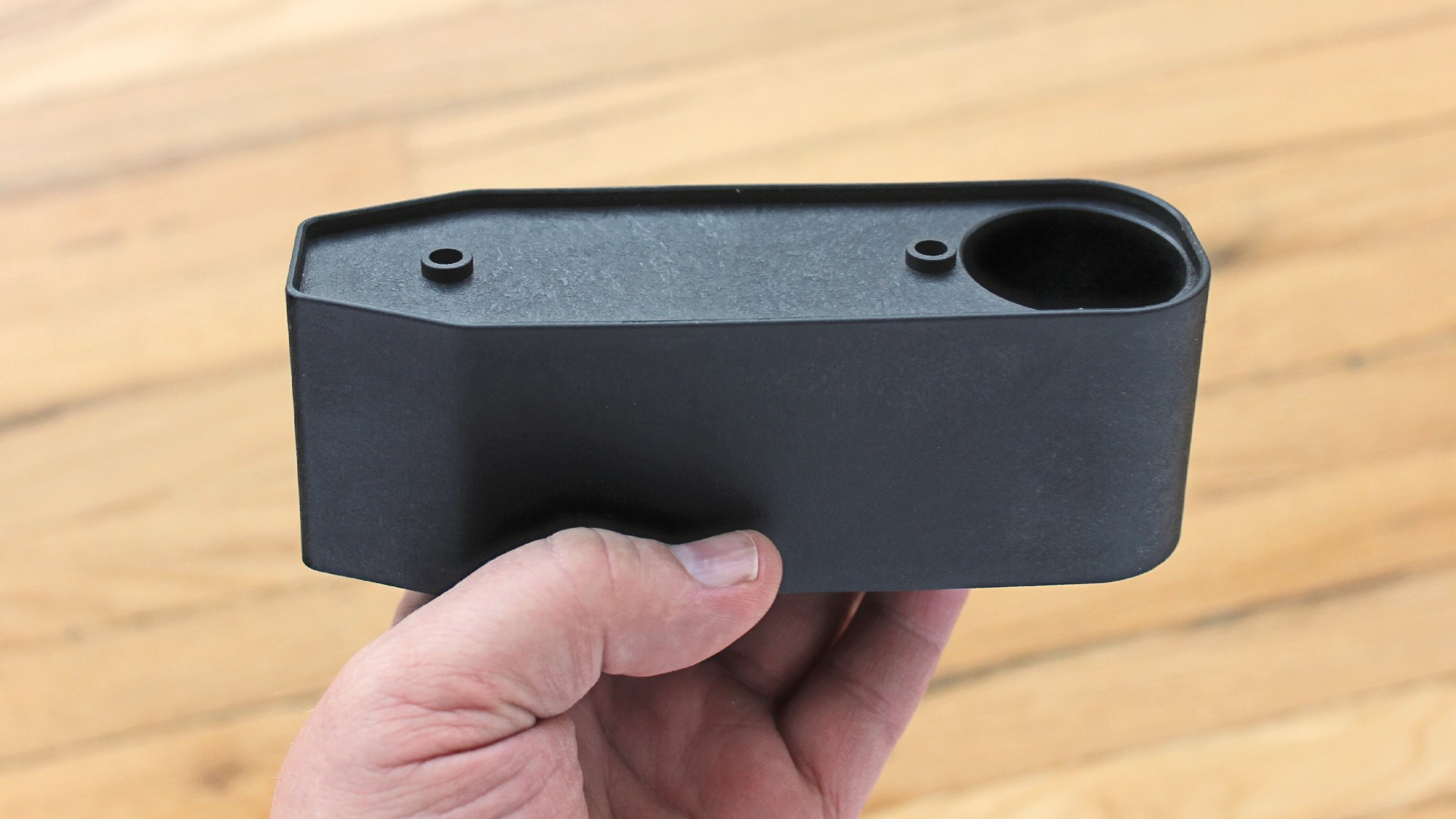 A3 Triad Bullpup stock spacer held in left hand with wood flooring background