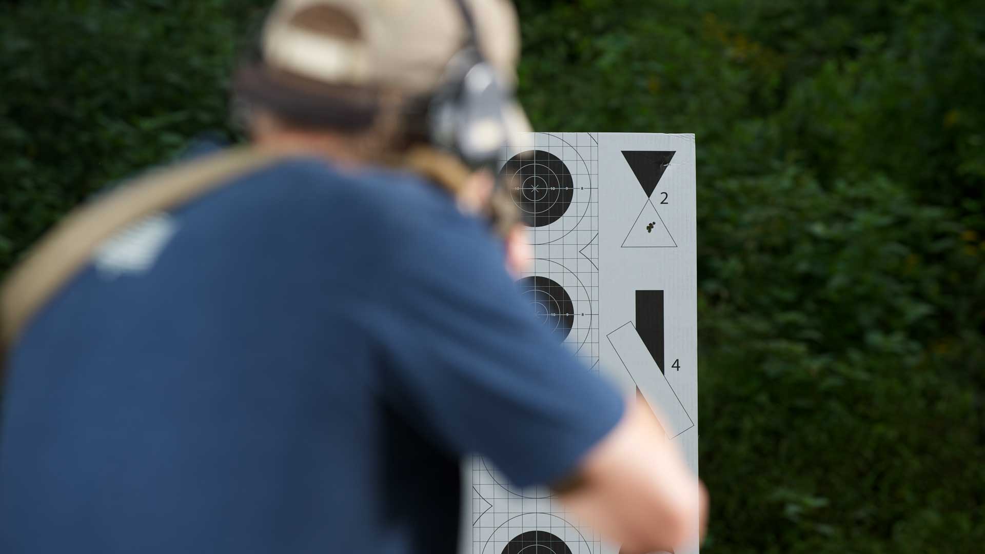 man blue shirt outdoors shooting rifle target