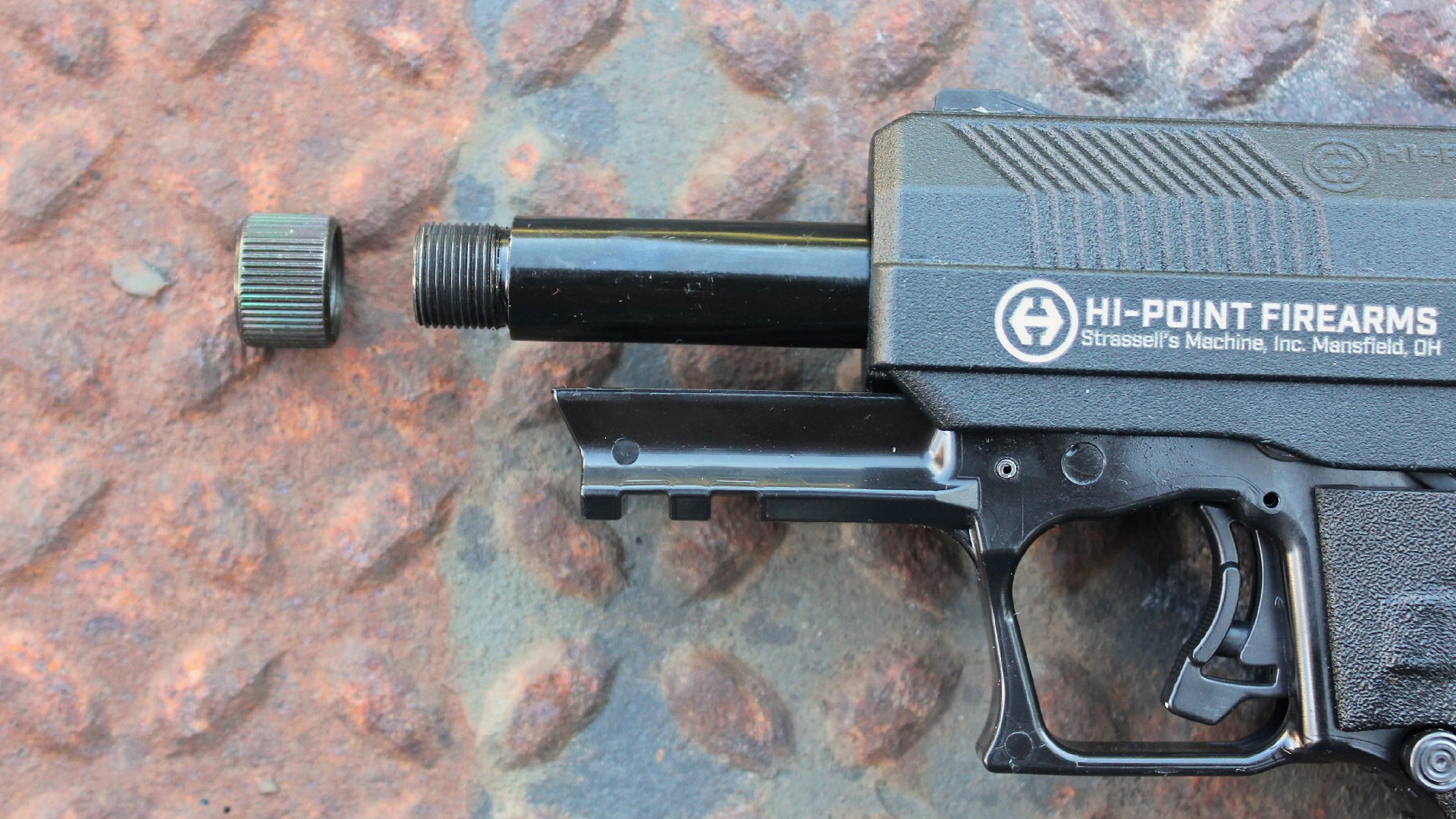Hi-Point Firearms YC9RD gun 9mm closeup slide locked back barrel exposed muzzle threads cap accessory rail rust background treadplate