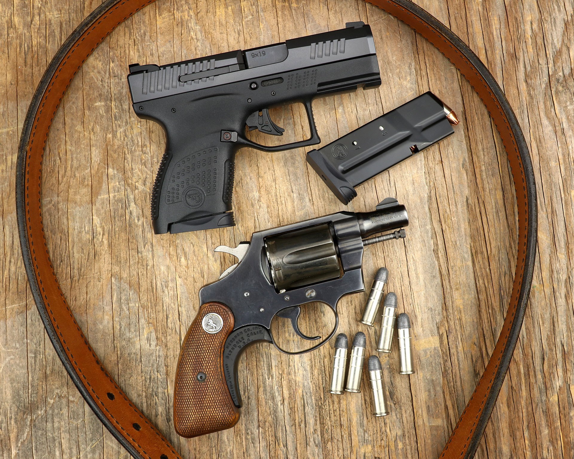 CZ P-10 M com pared with Colt revolver on tan background with brown leather belt, removed magazine and loose cartridges.