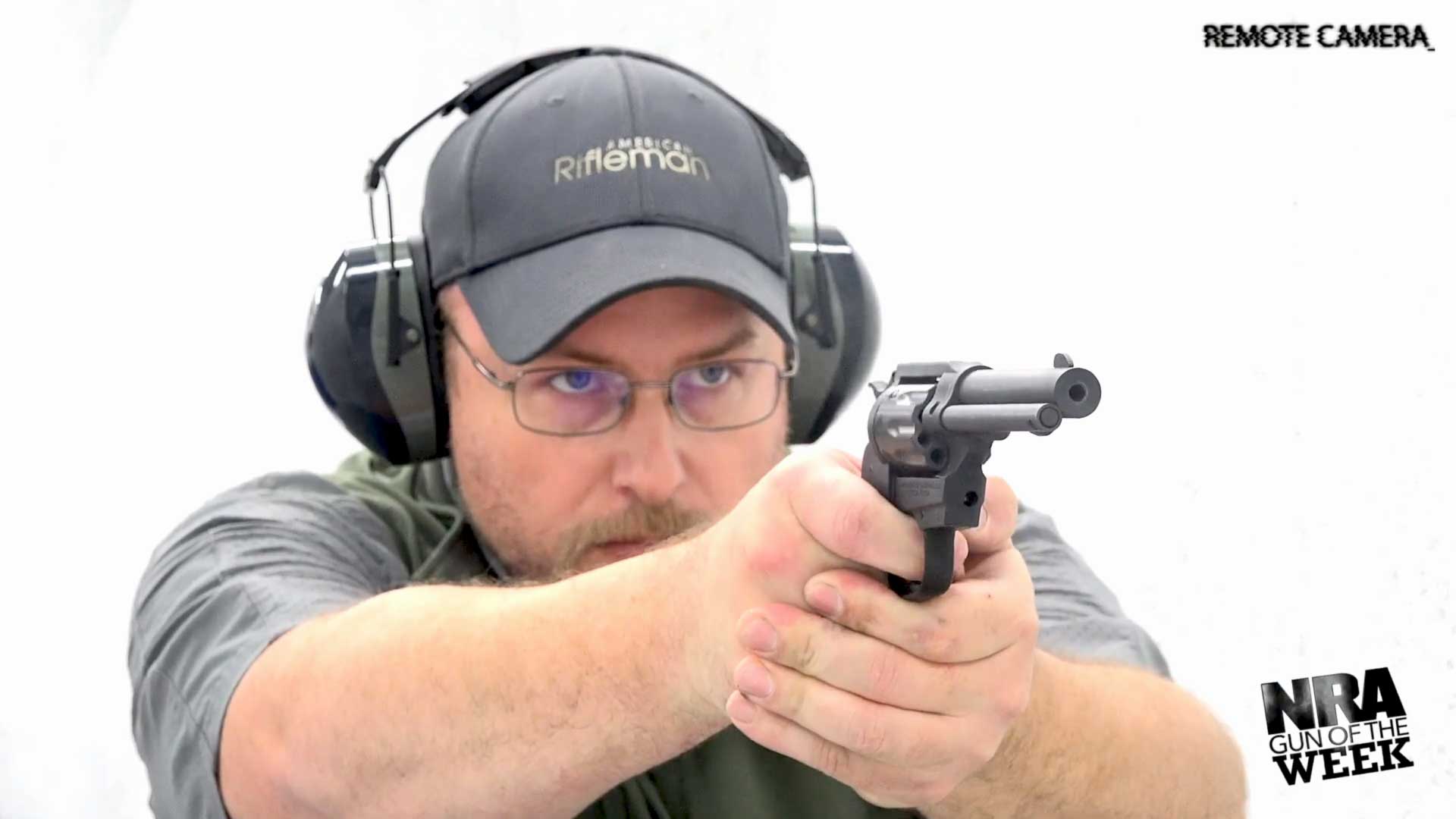 Man in gray hat shirt earmuffs protective gear shooting gun revovler black pistol text on image noting "NRA GUN OF THE WEEK REMOTE CAMERA"