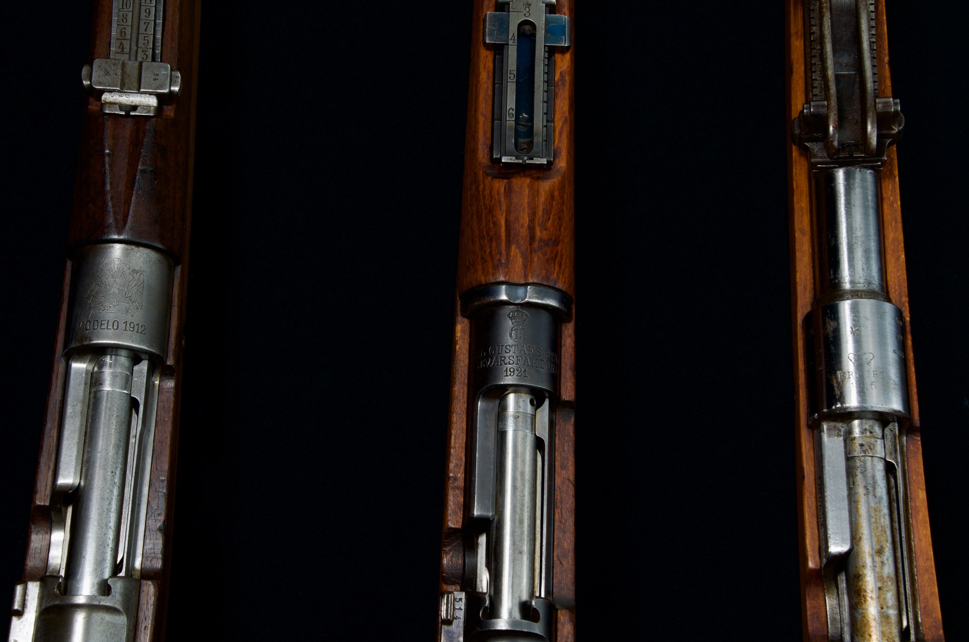 three mauser bolt-action rifles vertical row comparison wood metal black background