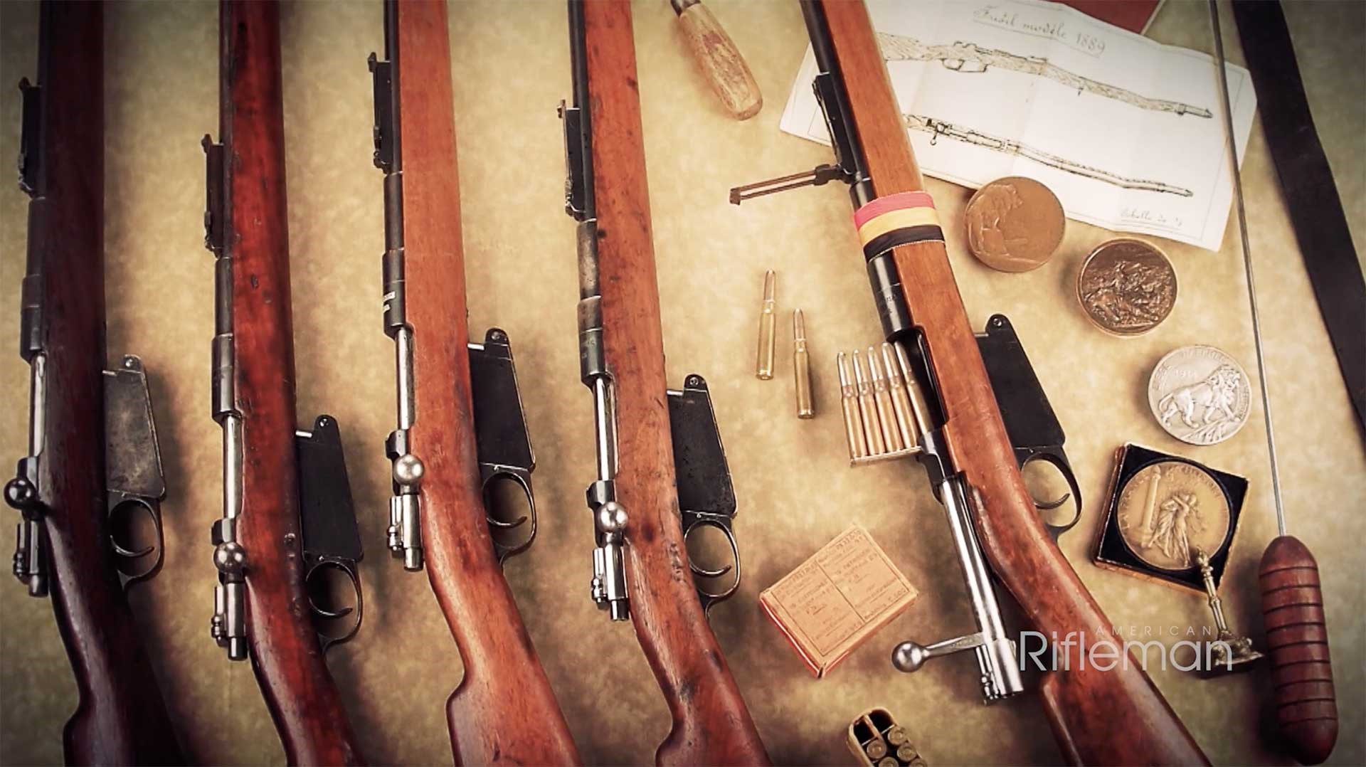 Five Model 1889 Belgian Mausers arrayed on a table, next to medals and ammunition boxes.