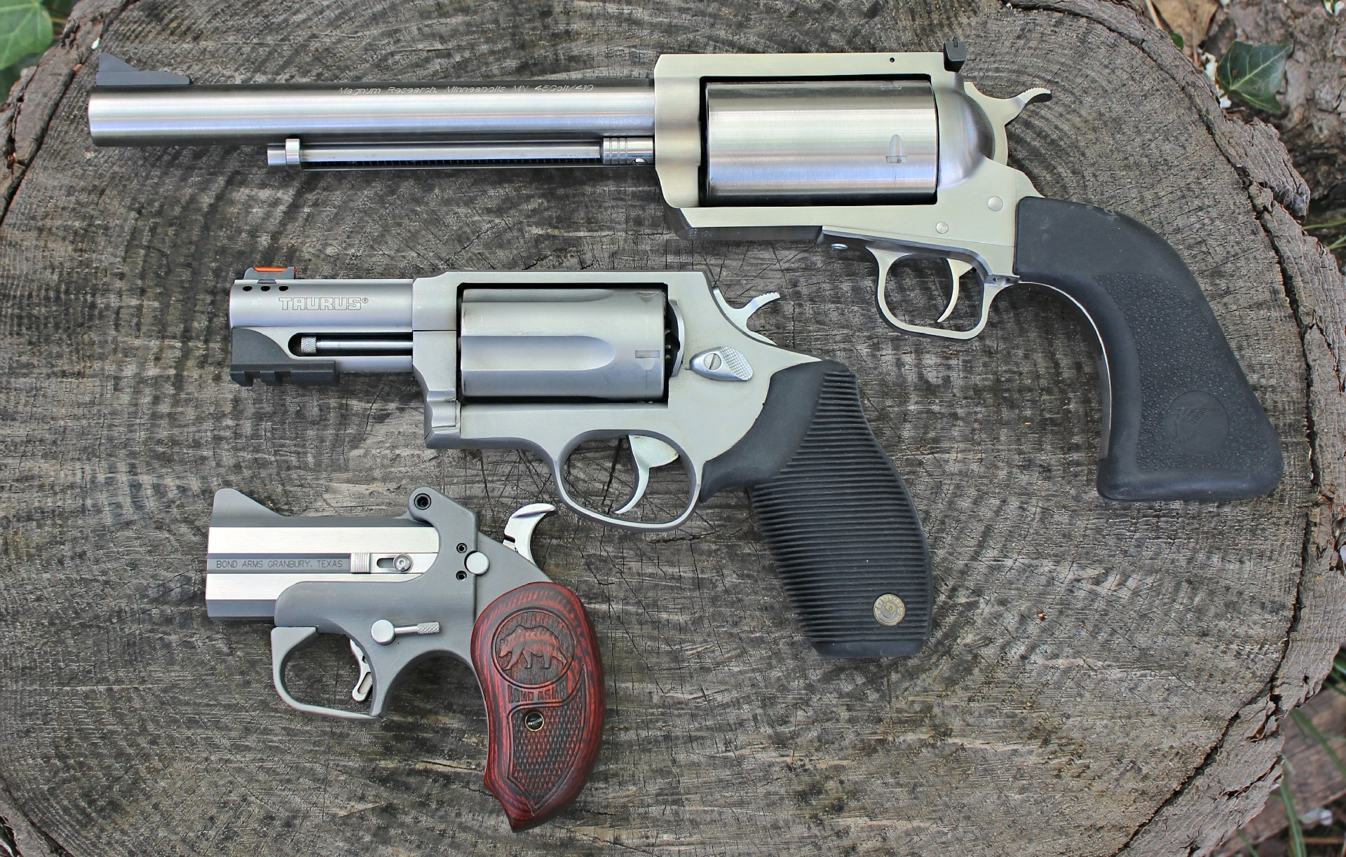 Handguns that can safely fire .410 bore shotshells are available in a variety of configurations three guns revolvers stainless steel black grips wood log resting overhead angle