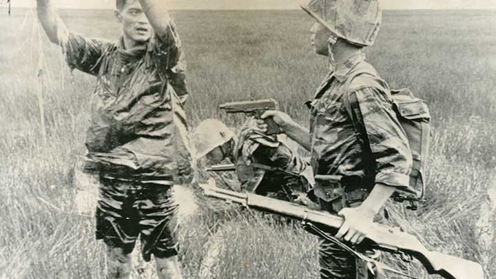 An ARVN soldier covers a Viet Cong prisoner with his M1911 pistol and M1 Garand rifle in 1962.