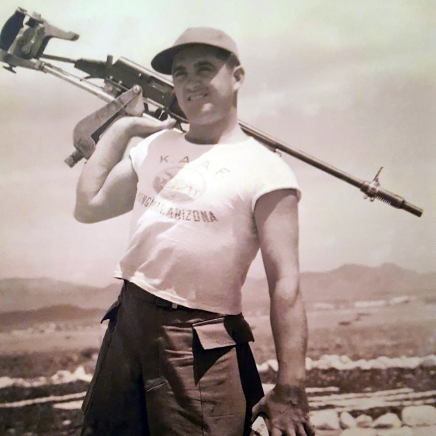 An aerial gunnery trainee posing with a long-barreled Remington Model 11 fixed with a Cutt&#x27;s compensator, raised aerial sights, and a chassis that simulates an aircraft machine gun mount.