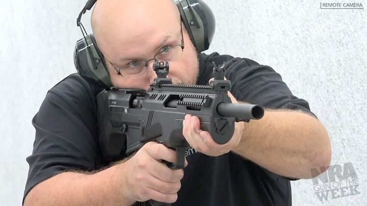 Man wearing protective shooting gear and black shirt holding a gun on a shooting range.