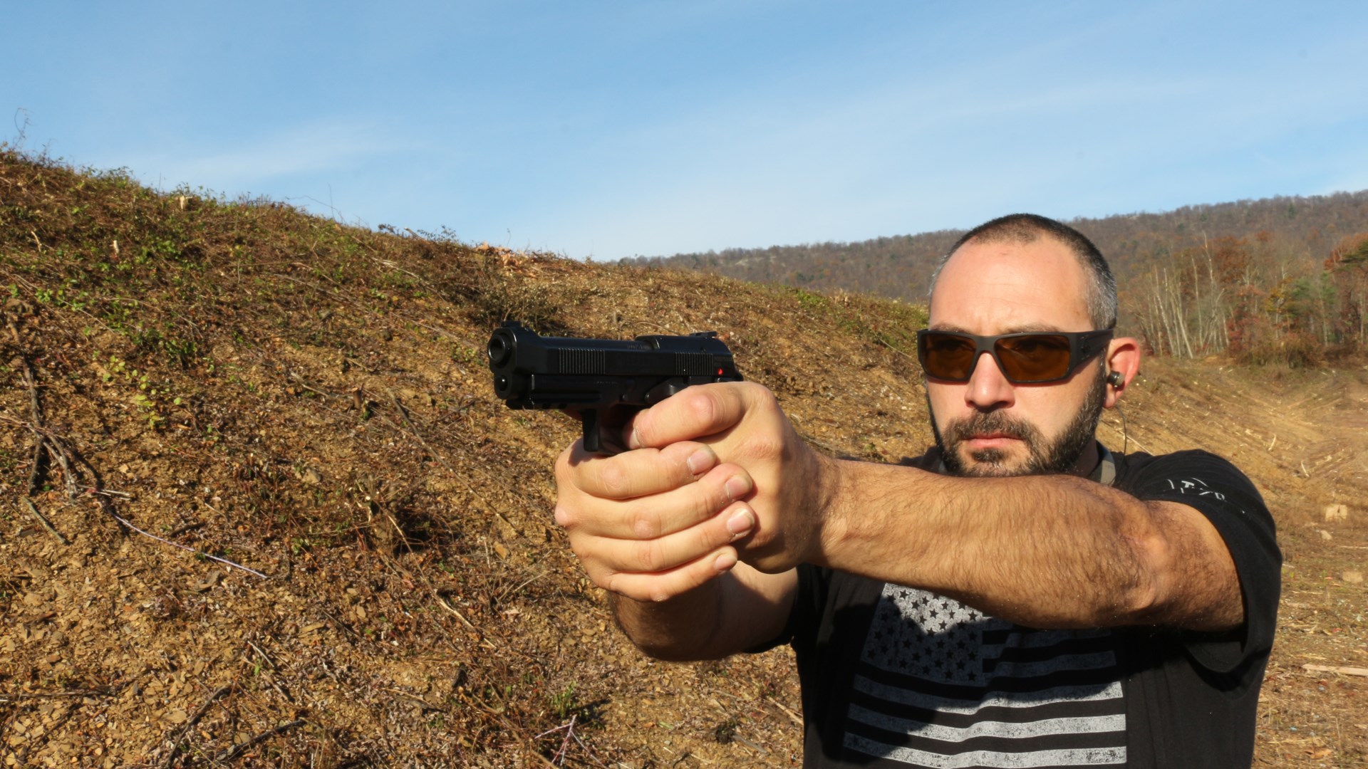 Author Frank Melloni standing outdoors in black american flag shirt wearing sunglasses holding Beretta 80X Cheetah 380 ACP pistol
