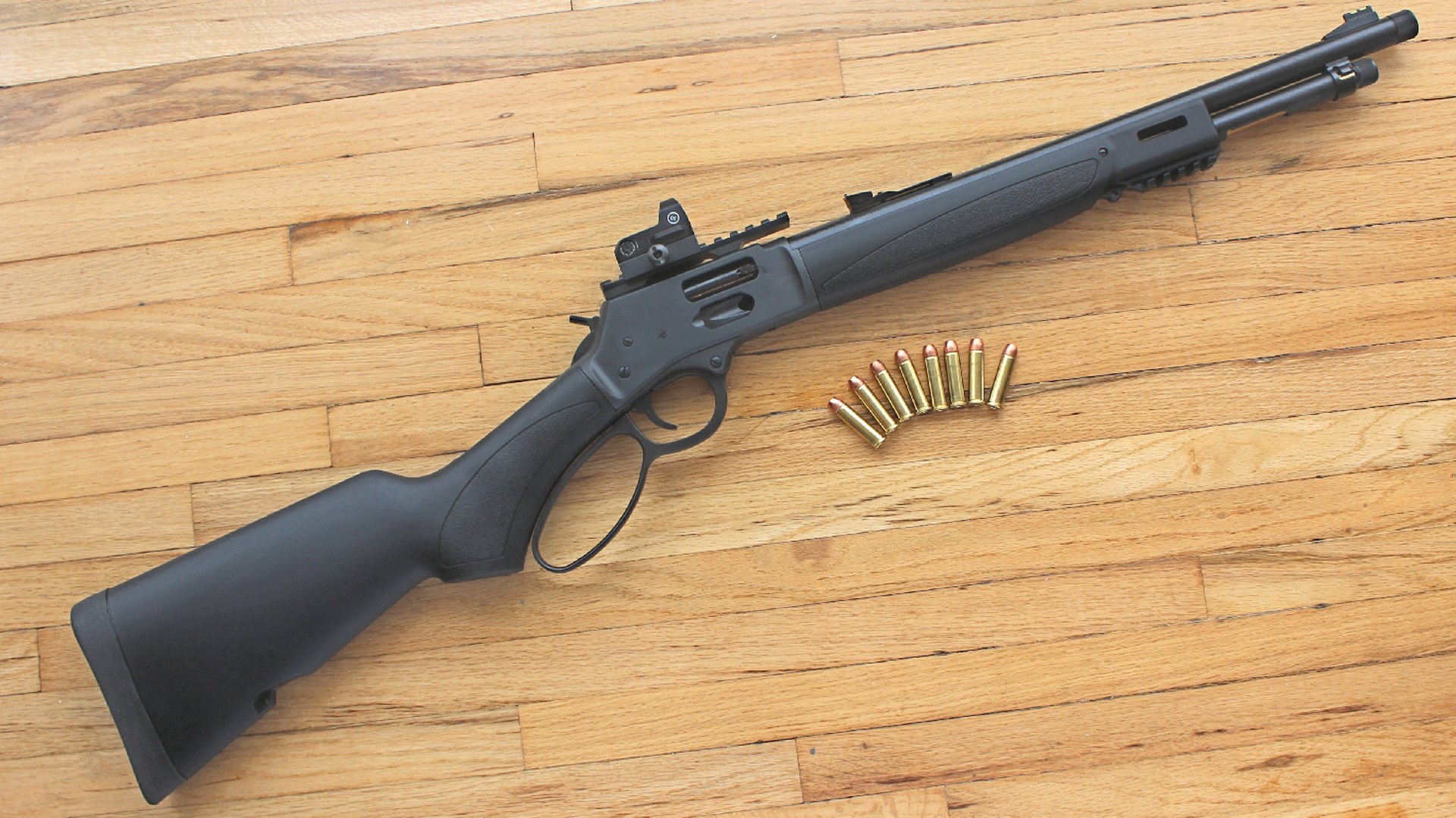 Henry Repeating Arms Lever-Action black-colored rifle with red-dot optic mounted on Picatinny rail shown on wood floor with ammunition