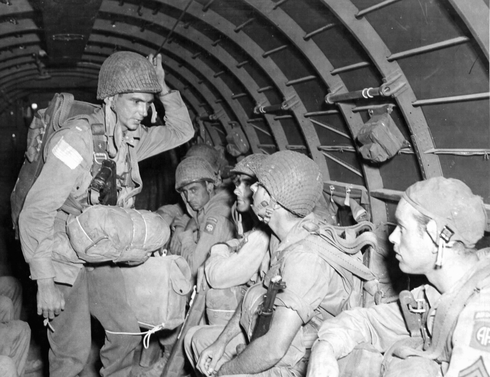 The first parachute assault of the 82nd Airborne Division came on July 9, 1943, over Sicily. The standing paratrooper carries an early M1A1 Carbine with a folding stock. NARA
