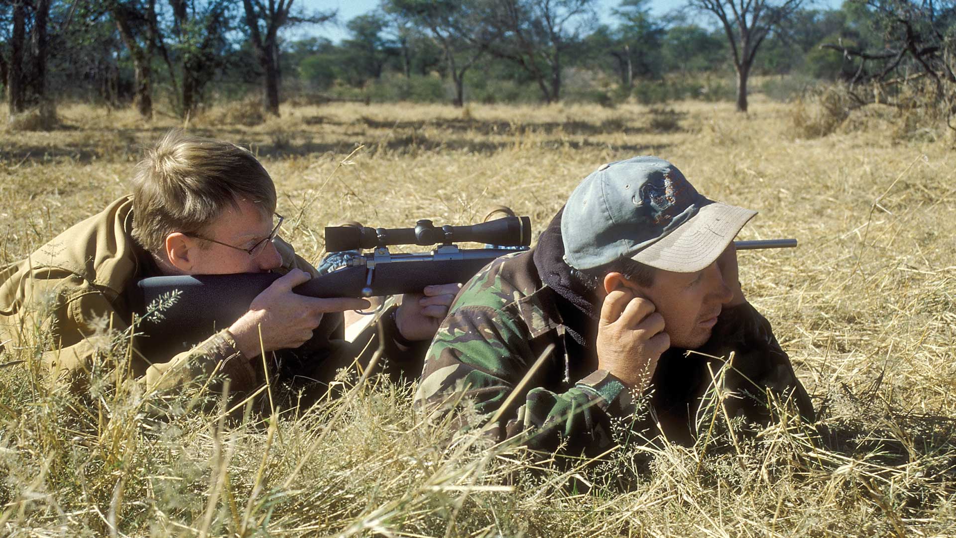 men hunters laying in grass rifle shooting outdoors field africa