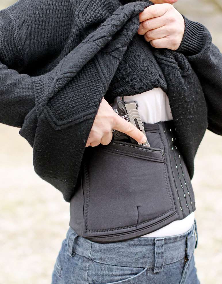 Woman in black sweater drawing a pistol from the concealment of a corset-style holster.