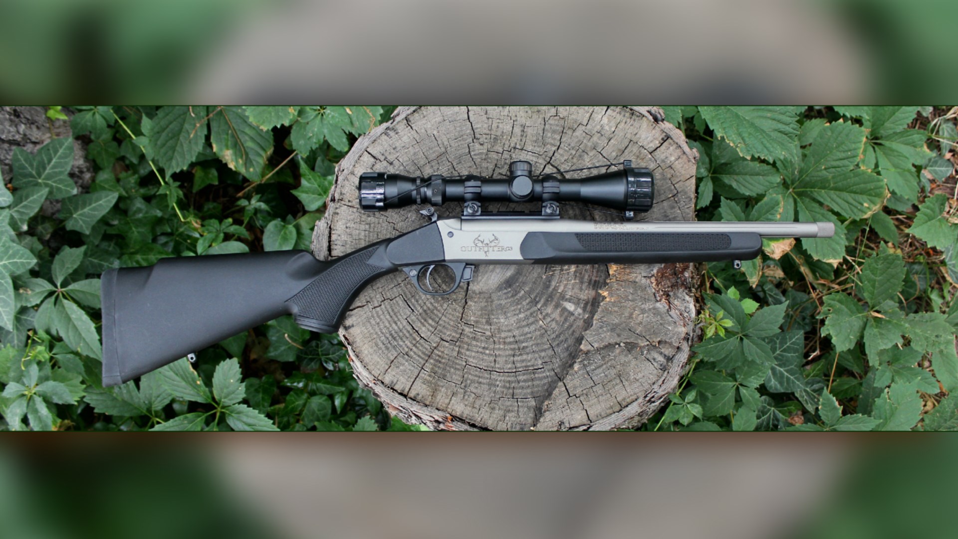 Right-side view Traditions Outfitter G3 single-shot rifle silver and black with riflescope resting on log with green leaves surrounding ghosted blurr overlay