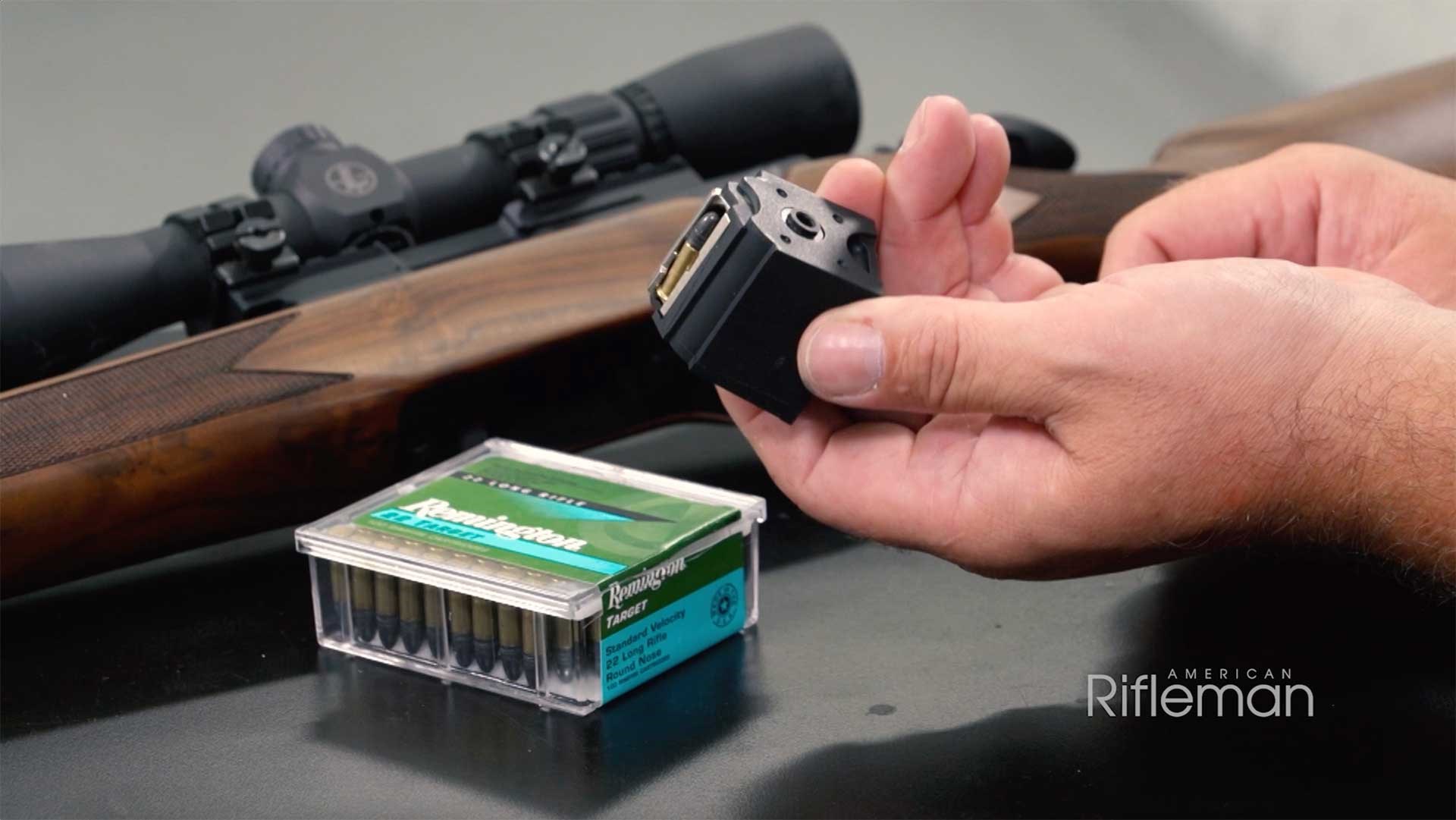 Man holding a rotary magazine next to a box of .22 Long Rifle ammunition with a Springfield Model 2020 Rimfire Classic rifle in the background.