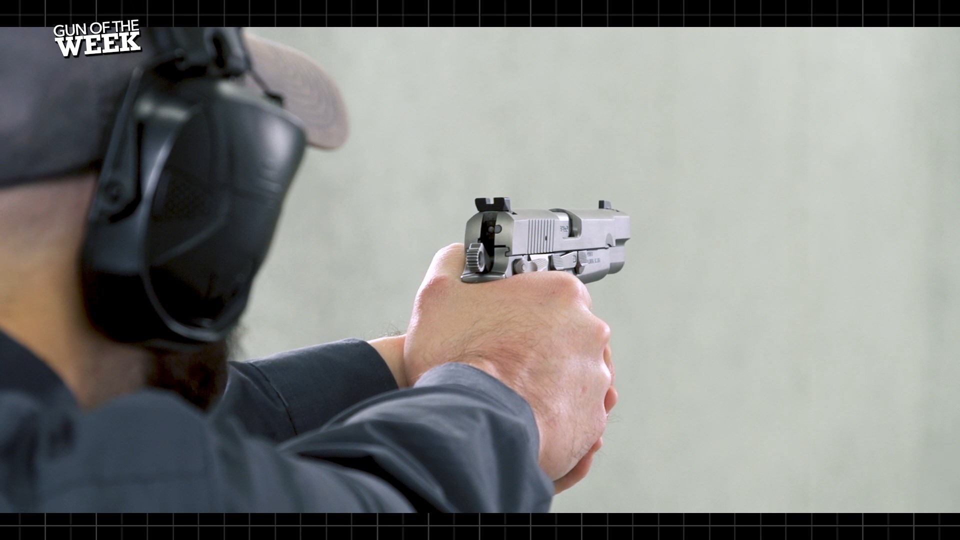 over-the-shoulder view of man shooting fn america high power pistol stainless steel gun 9 mm indoor