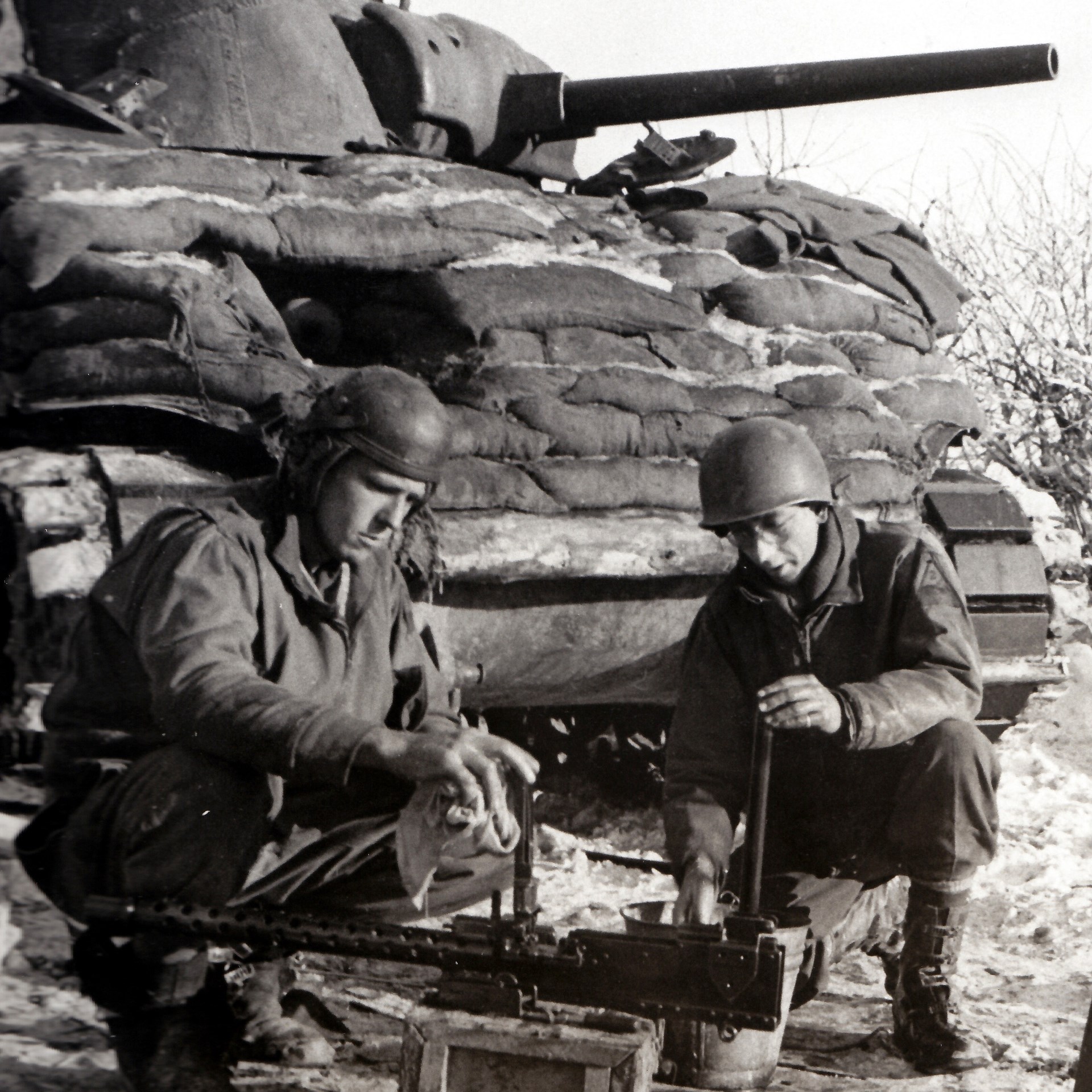 Tankers of the 2nd Armored Division clean one of their vehicle’s Browning M1919 .30 caliber MG. Note the sandbags on the Sherman tank’s glacis plate, improvised protection against German hollow-charge anti-tank weapons.