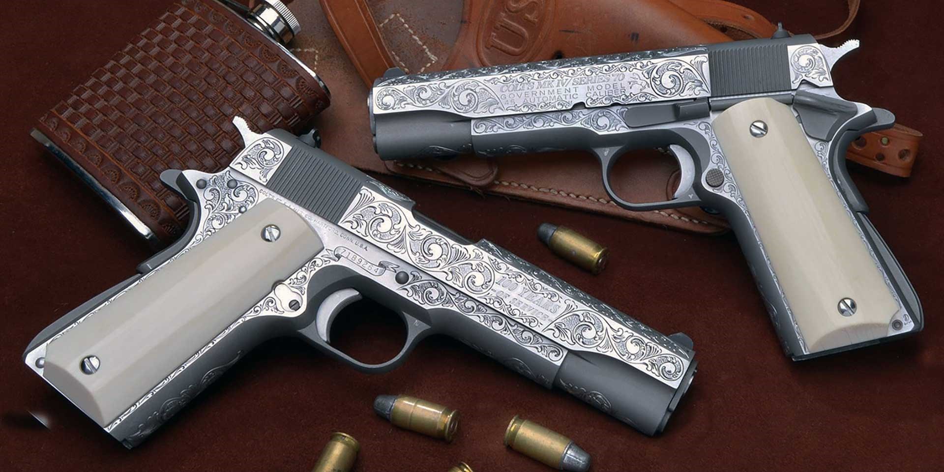 Two Colt M1911 handguns with highly figured engraving on their metal components.