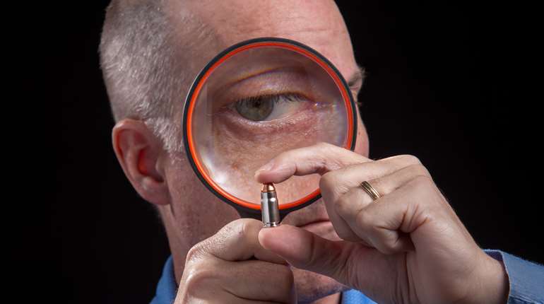 man inspecting a cartridge with a magnifying glass