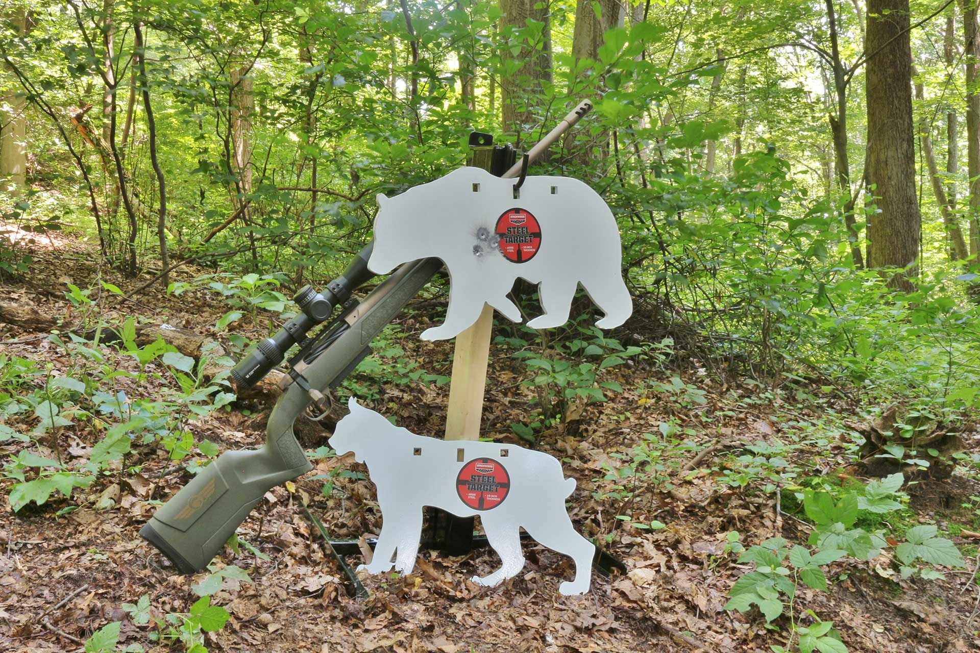 Hanging white steel targets shaped like animals next to a rifle in the woods.