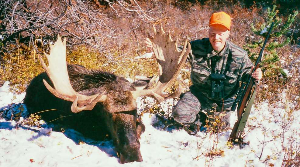 Craig Boddington with Moose outdoors snow on ground hunter with rifle