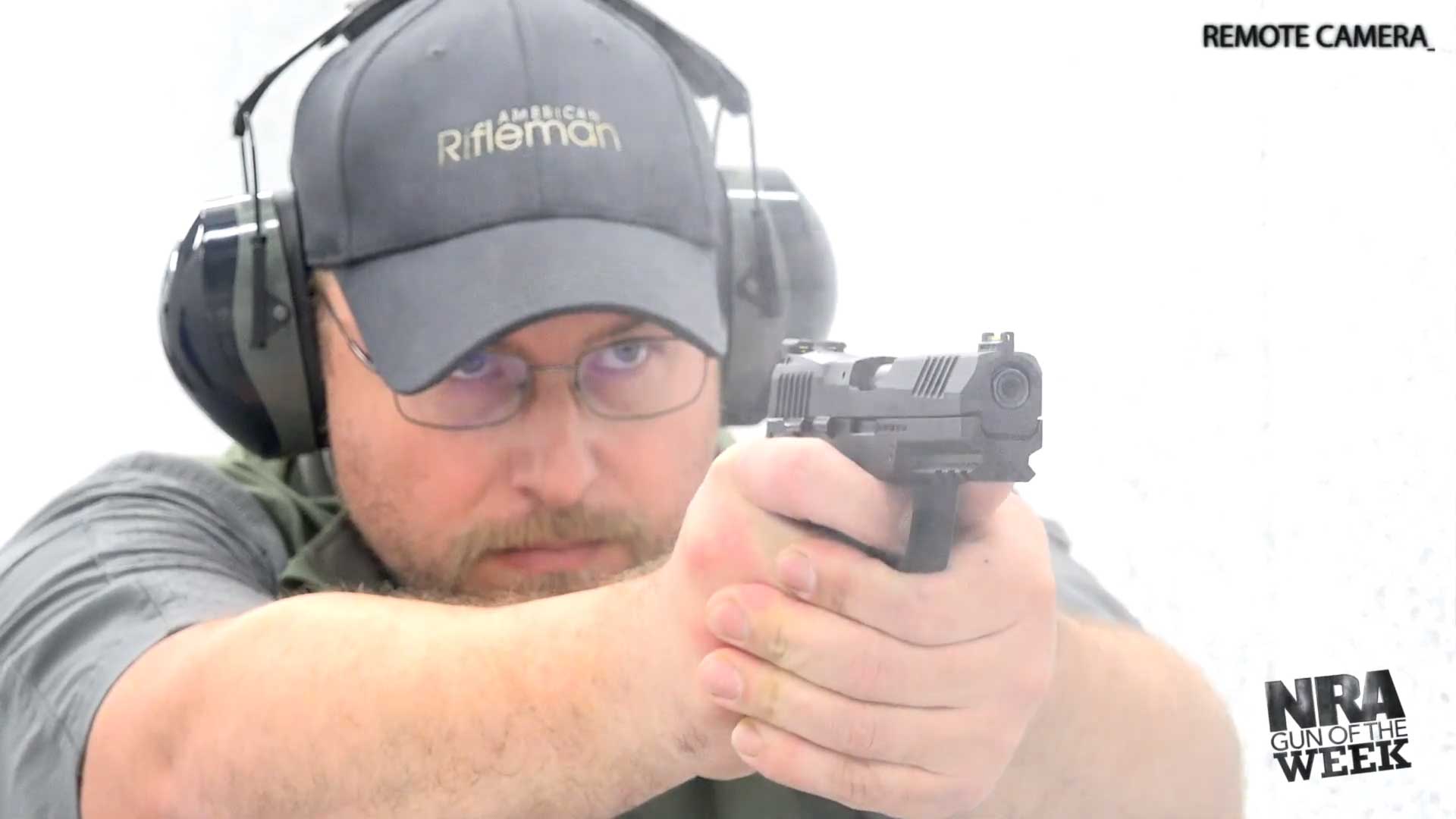 man wearing gray hat, shirt and earmuffs shooting gun pistol handgun black semi-automatic SIG SAUER P322 gun smoke remote camera shooting range