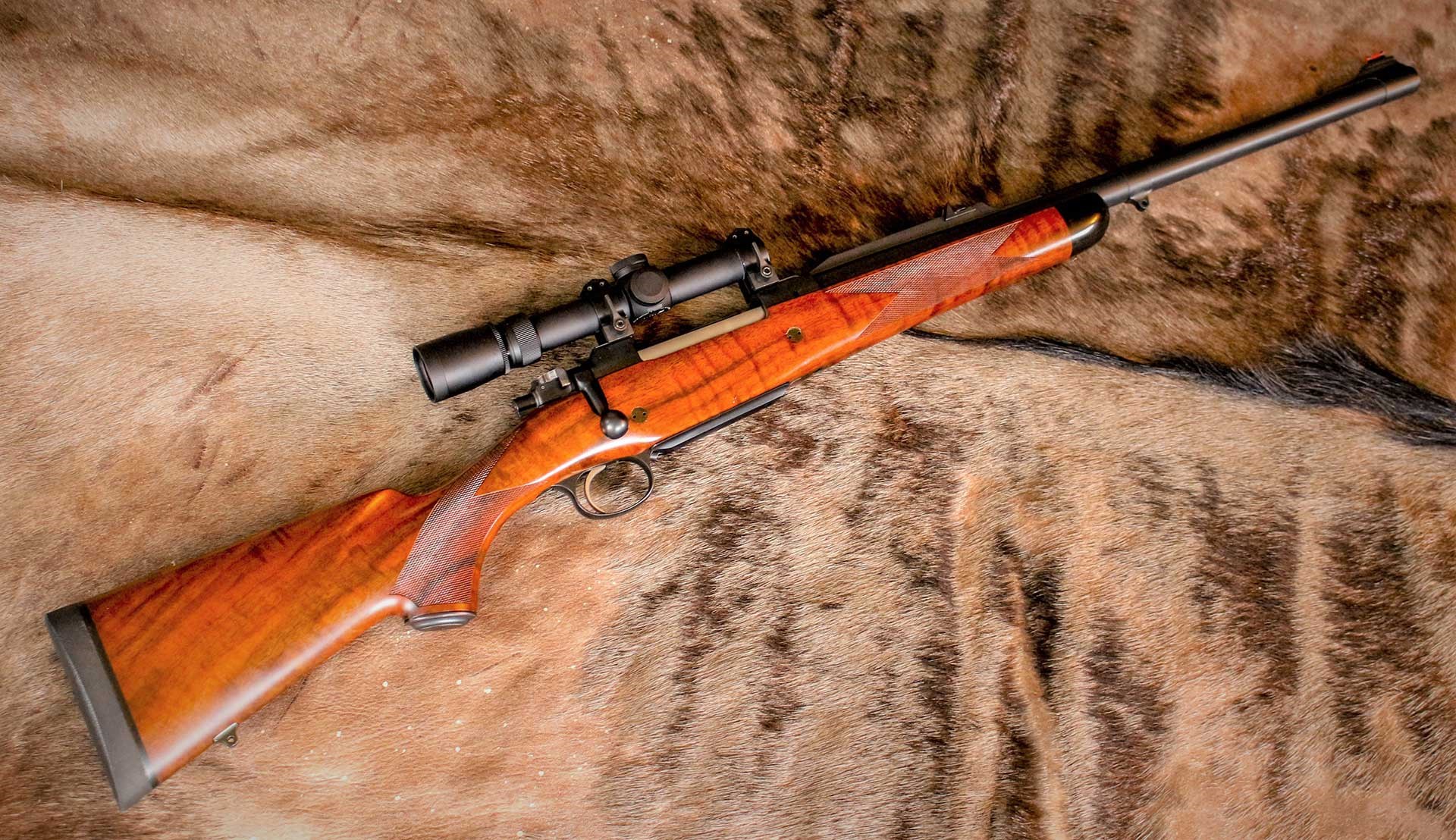 A .416 Rigby hunting rifle, shown full length, lying on a deerskin background.