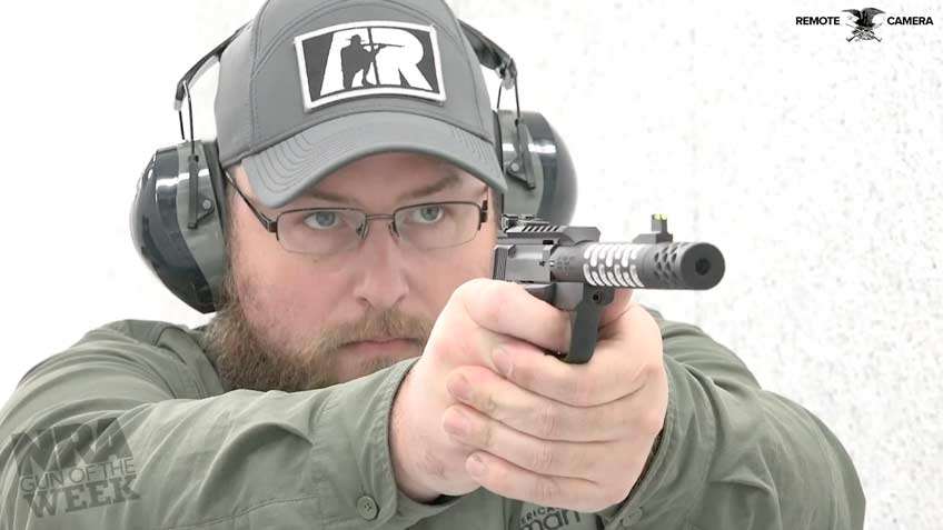 Man wearing ballcap, ear muffs and classes shooting a black pistol with text on image noting remote camera