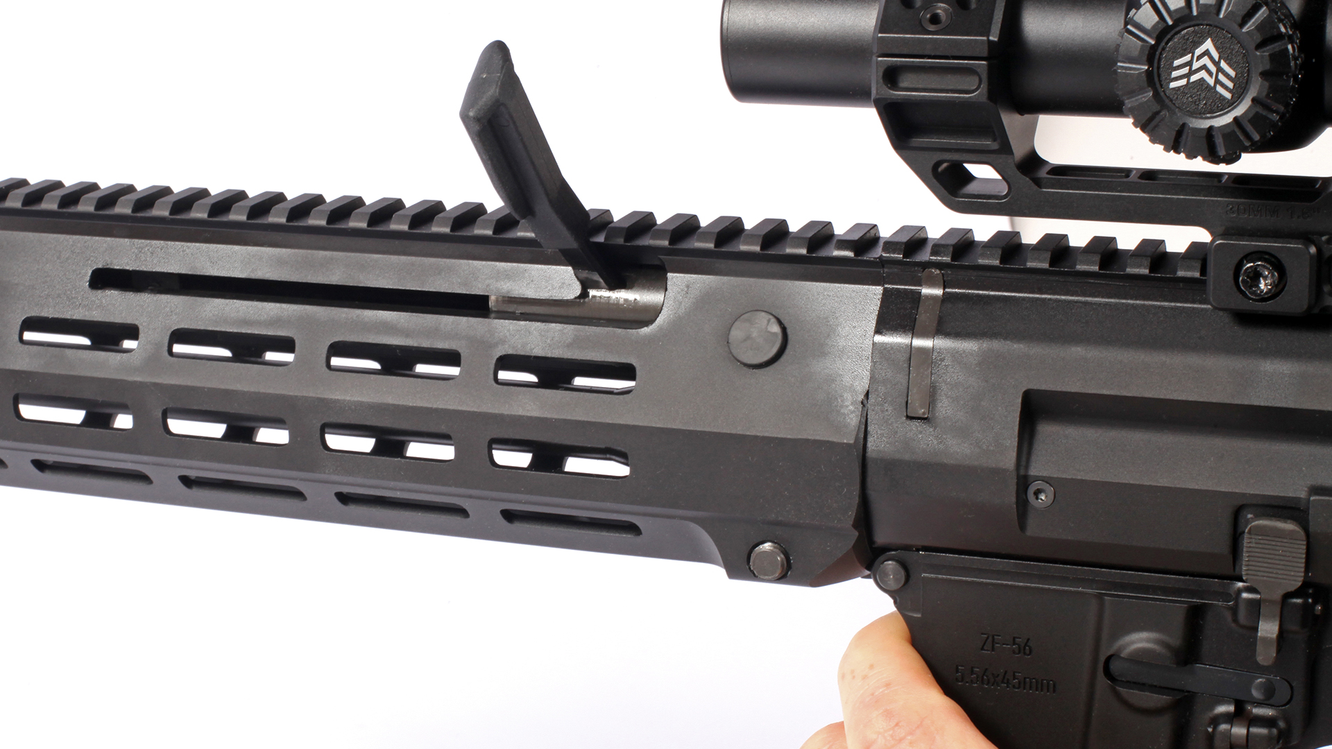 Charging handle locked rear position of handguard with Picatinny rail shown on white background with riflescope attached