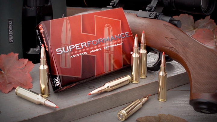 Hornady Superformance ammuntion box shown with loose ammo, rifle and binoculars.