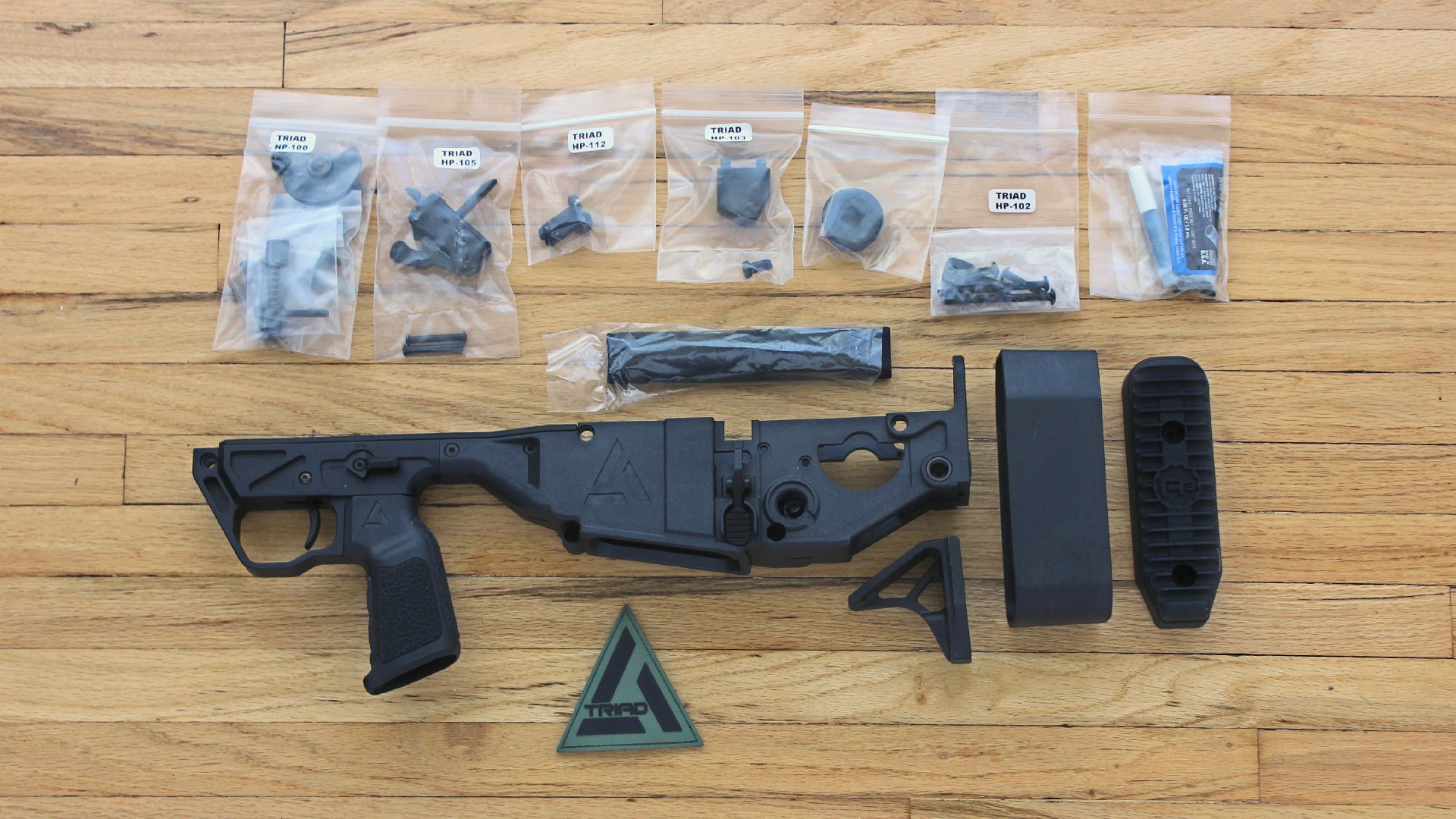 A3 Triad Bullpup conversion kit with parts spread on wood floor left-side view bullpup chassis and aero precision lower recevier