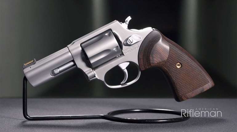 Taurus Executive Grade revolver left-side view stainless steel gun with walnut grip positioned on black wire stand