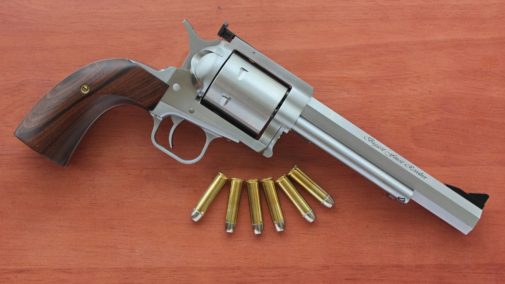 Right-side view angled silver stainless steel Magnum Research Biggest Finest Revolver gun brass .357 Mag ammunition on wood table