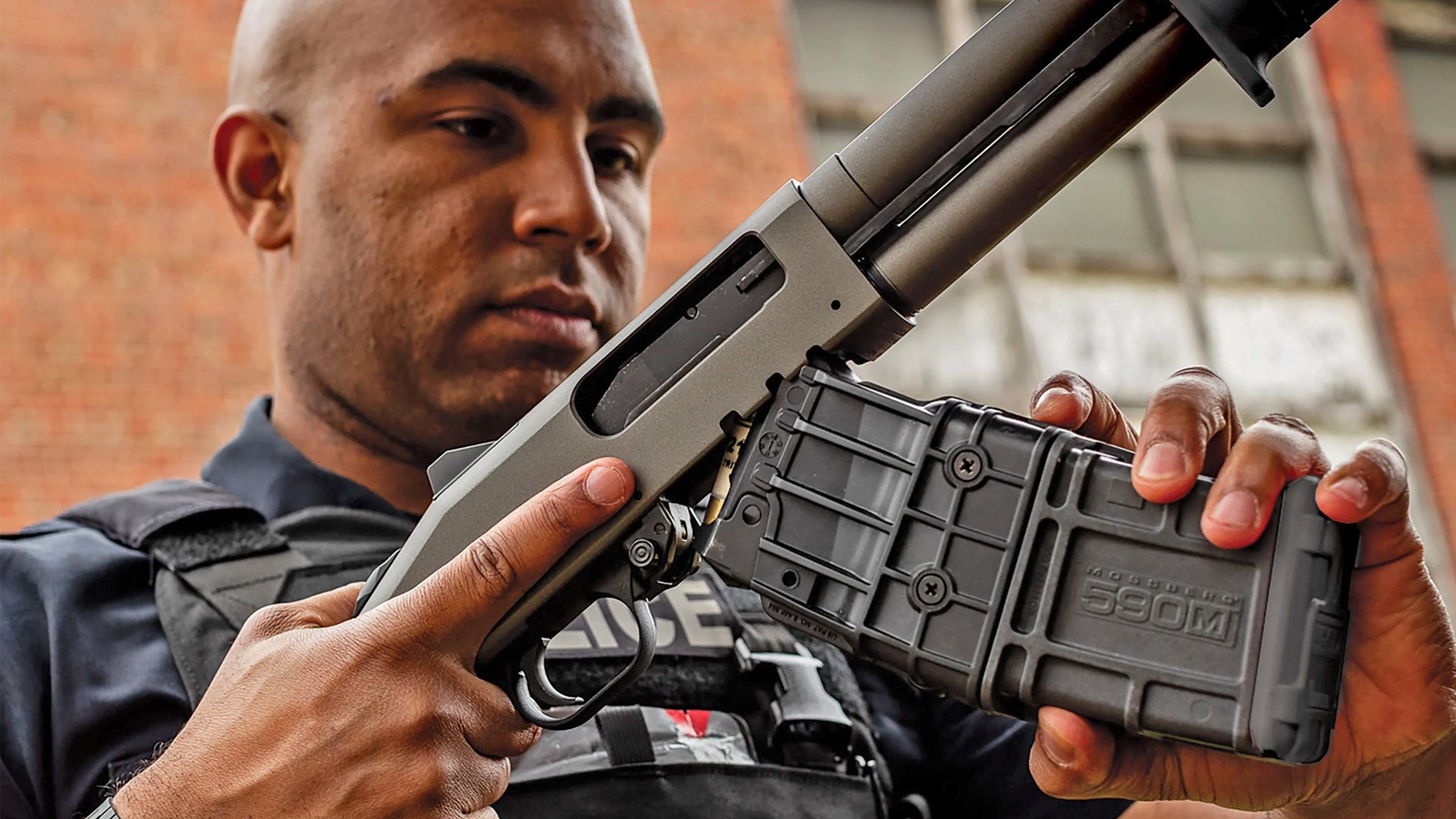 Man inserting a box magazine into a Mossberg 590M shotgun.