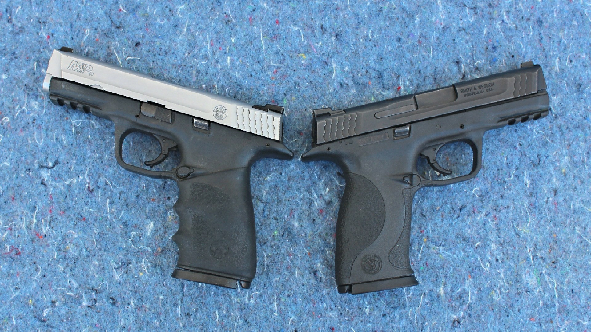 Two Smith & Wesson M&P guns 40 and 45 cal opposing view left two-tone stainless steel and black right gun all black shown on blue background