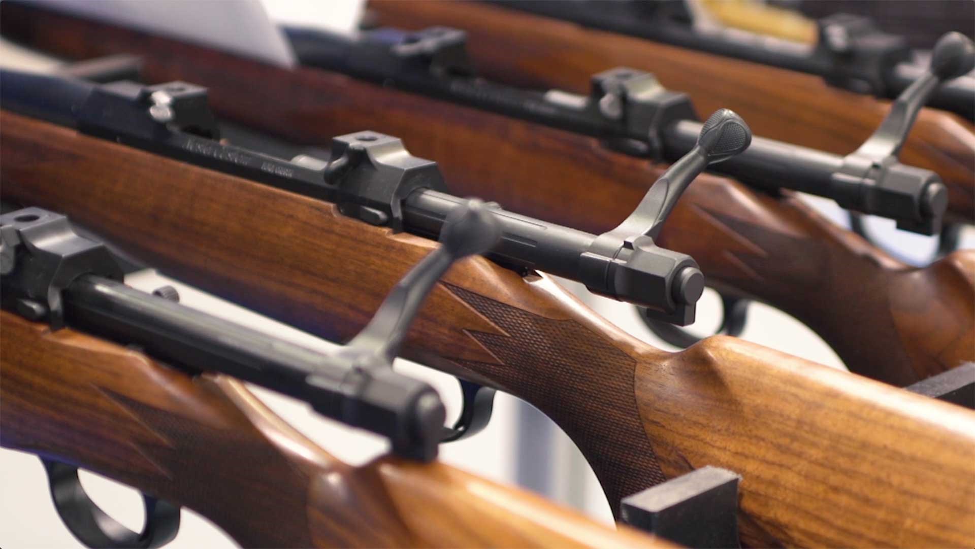 A group of wood-stocked hunting rifles with their bolts open for inspection.