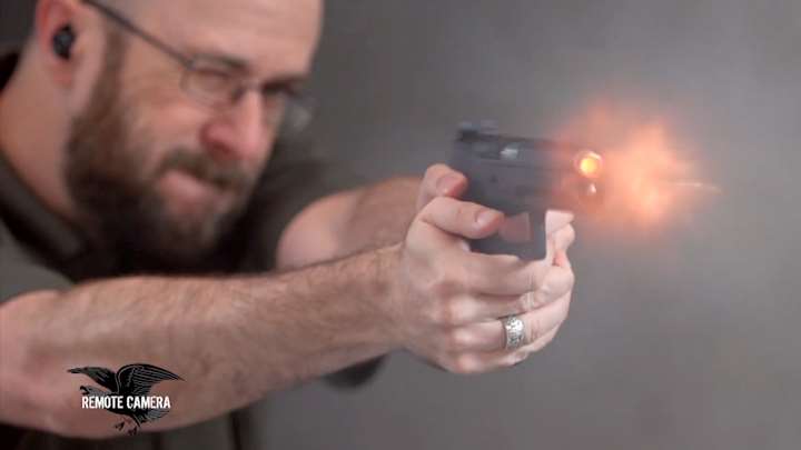 Man shooting handgun on range and blast coming from the barrel.