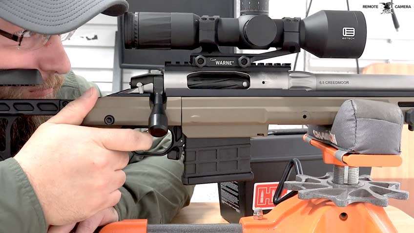 Man ballcap white hand on tan rifle with black scope orange rest