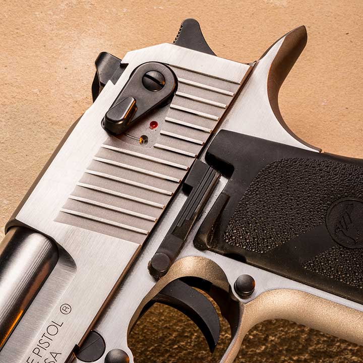 The left-side constrols of the Magnum Research Desert Eagle on a tan background, showing safety, slide stop, magazine release and trigger.