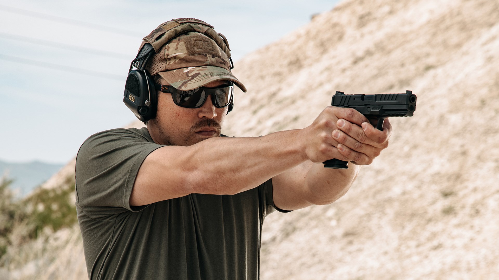 A man with hat and ear protection aiming a black Springfield Armory Echelon in a desert.