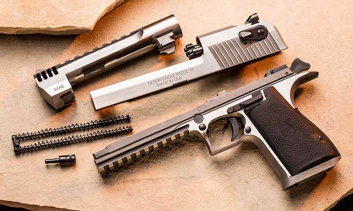 Disassembled Magnum Research Desert Eagle lying on a sand background, showing the frame, slide, barrel and related components.