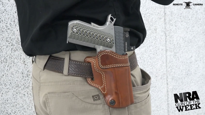 Pistol in brown holster tan pants black shirt text on image