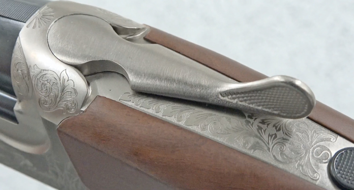 Silver receiver tang and top lever of shotgun with wood stock.