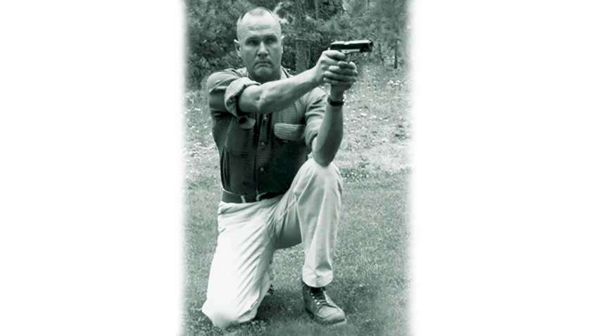 Jeff Cooper kneeling on grass, demonstrating the Weaver Stance.